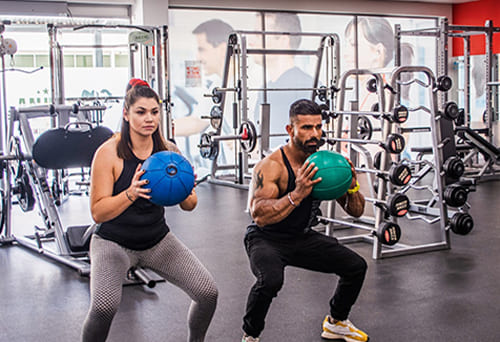 People performing squats with medicine balls in a gym