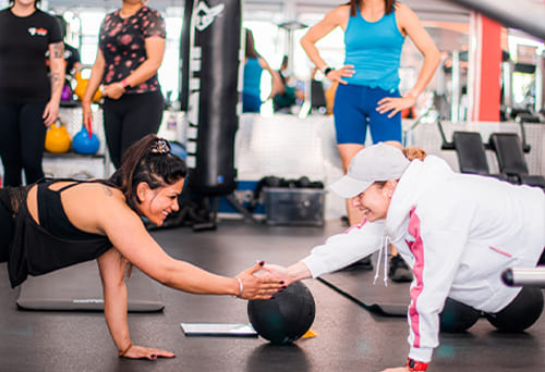 Two people performing a fitness challenge in the gym, touching hands while holding medicine balls