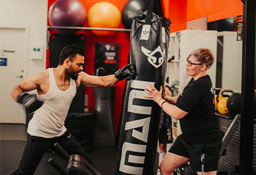Two people boxing on a punching bag in the gym